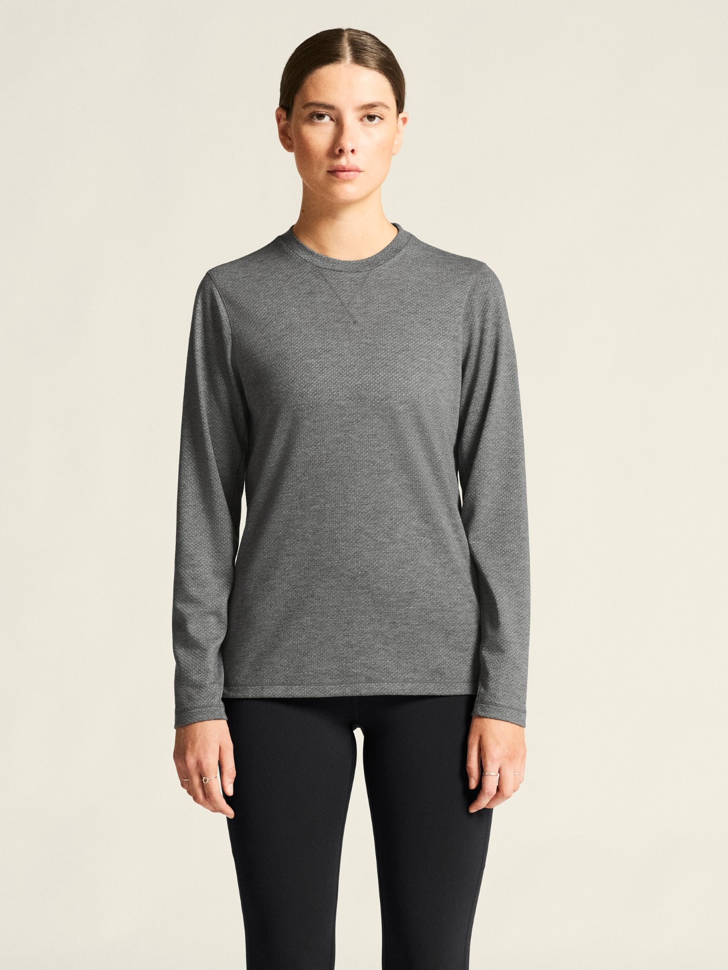 Woman wearing a gray long-sleeve shirt and black pants on a beige background