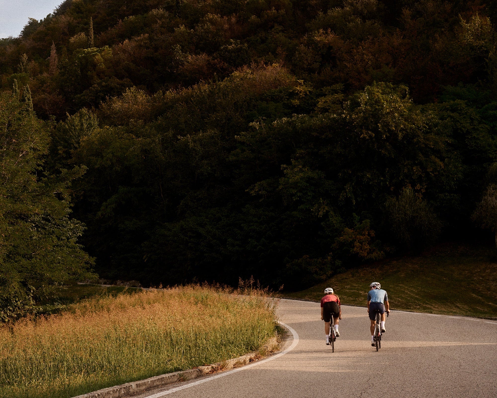 Two people biking on the road on the side of a large hill