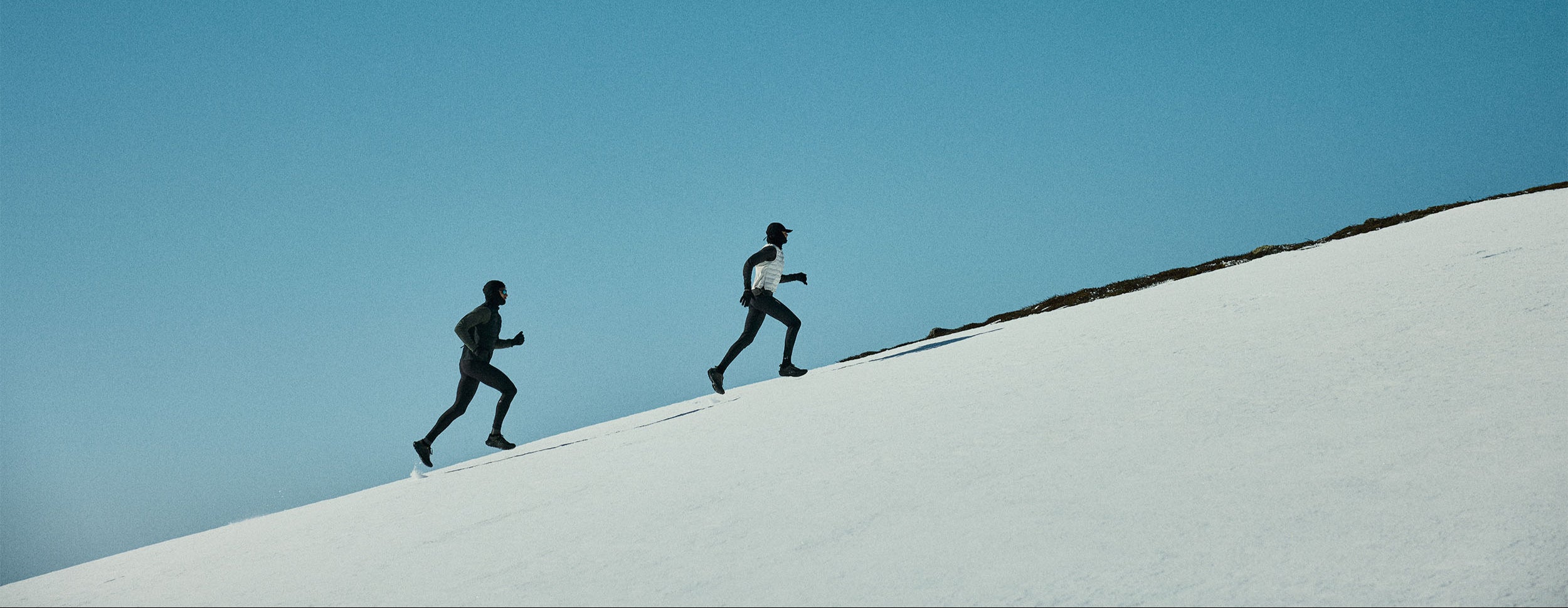 Two people running on a white snow under a clear blue sky