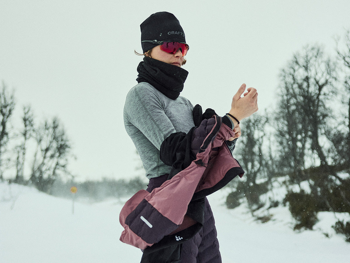 Personne vêtue d'habits d'hiver, avec une écharpe et des lunettes de soleil, debout dans un paysage enneigé.