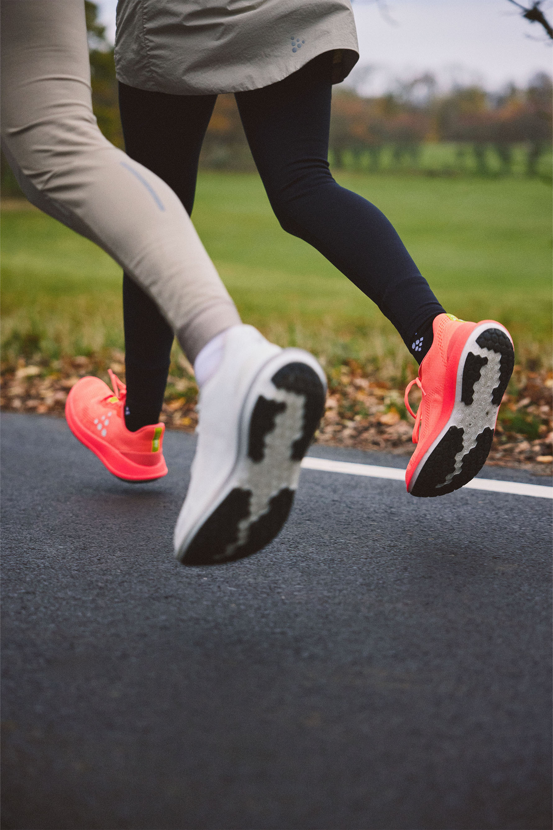 Two pairs of legs in running shoes on a road with a blurred natural background