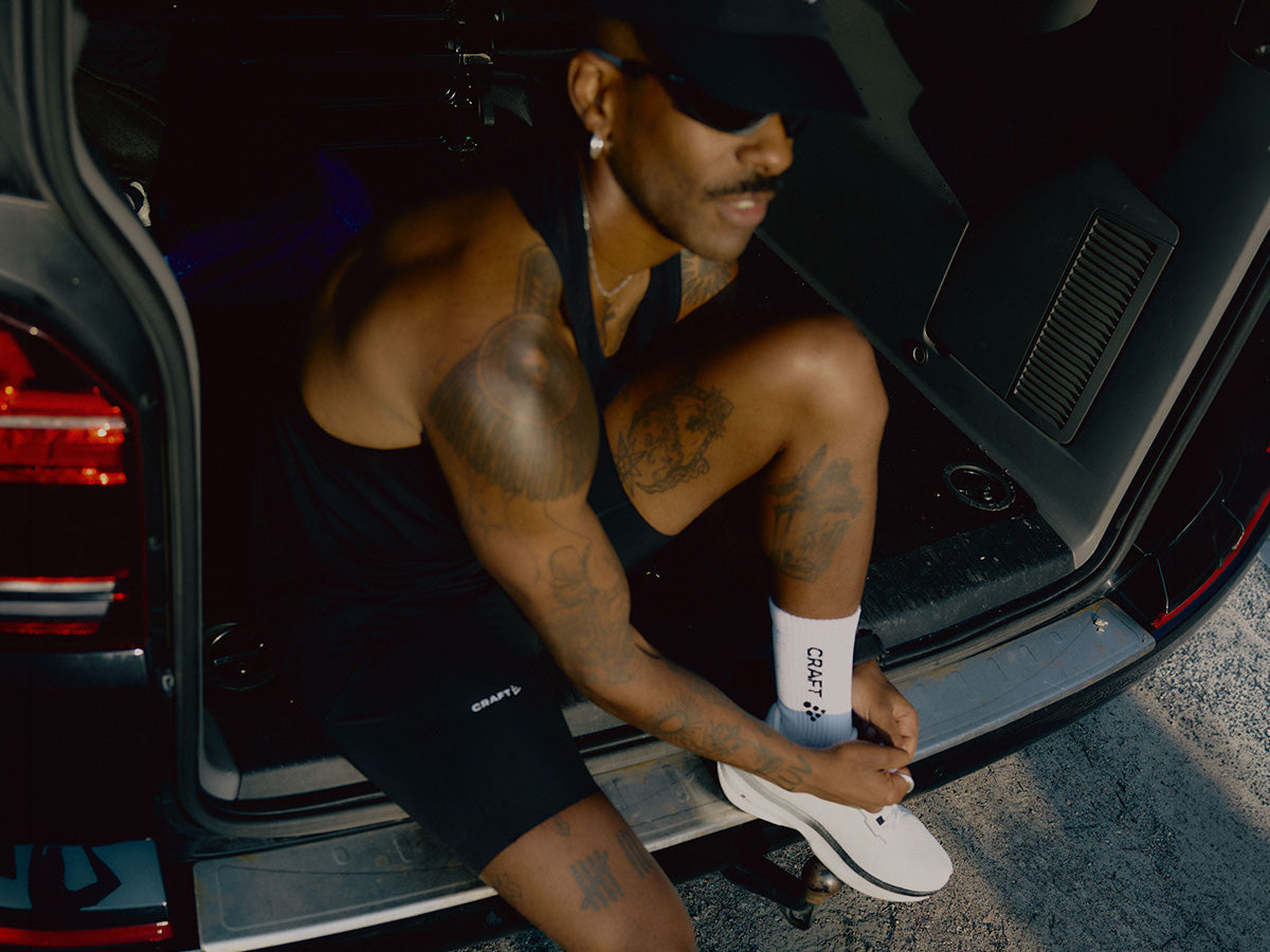 Man sitting in the back of a car wearing a black tank top and shorts.