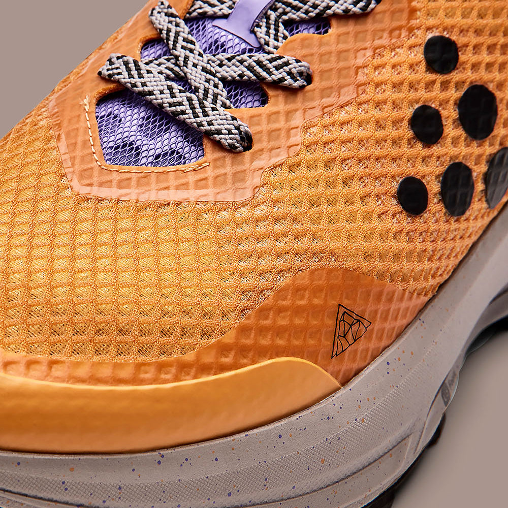 Gros plan sur une chaussure de sport orange avec une semelle texturée et le logo de la marque.