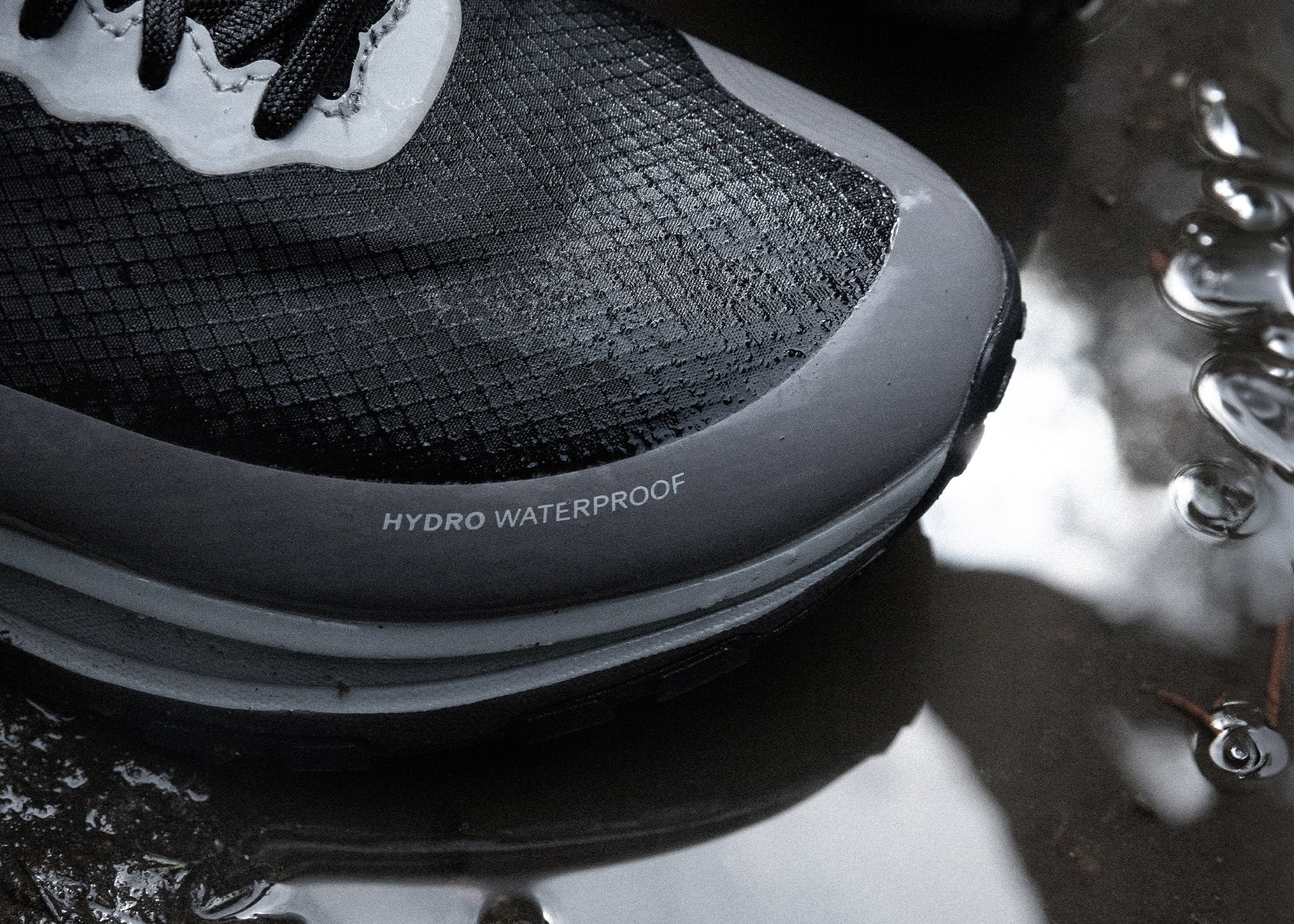 Toe of black running shoe on water puddle.