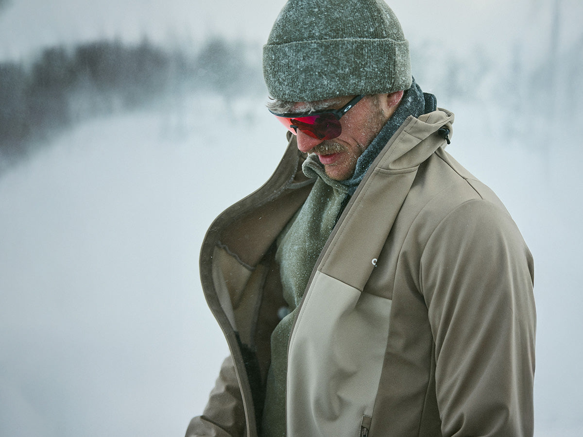 Man wearing a winter coat, hat, and sunglasses in a snowy landscape