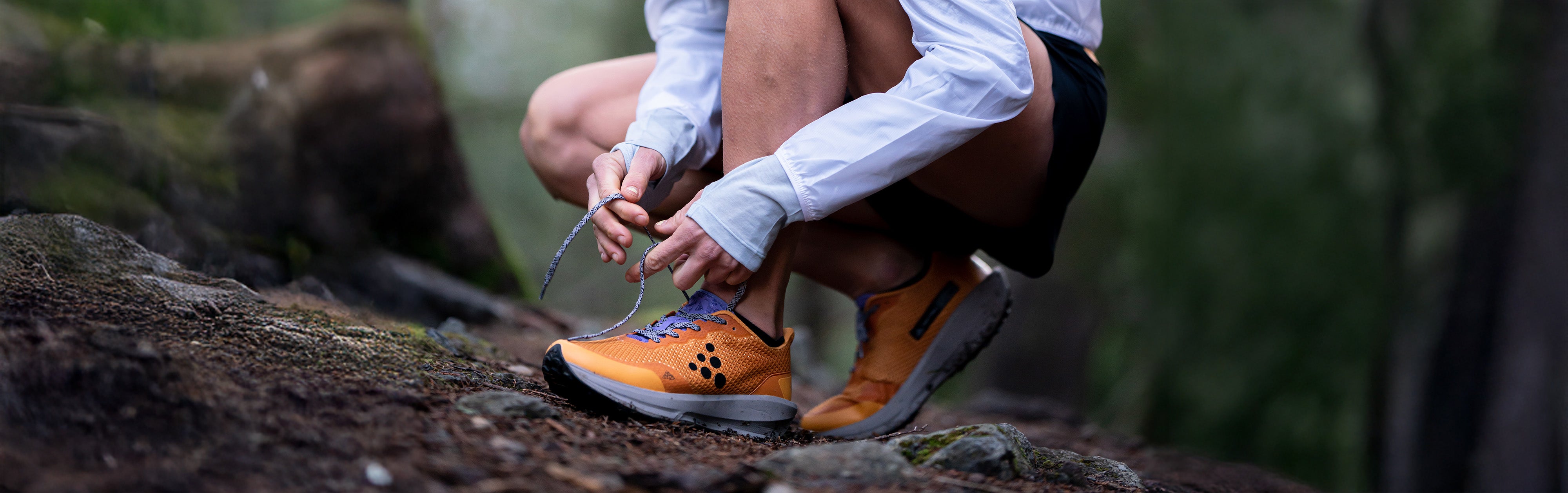 Personne laçant ses chaussures de randonnée sur un sentier rocailleux avec un arrière-plan naturel flou