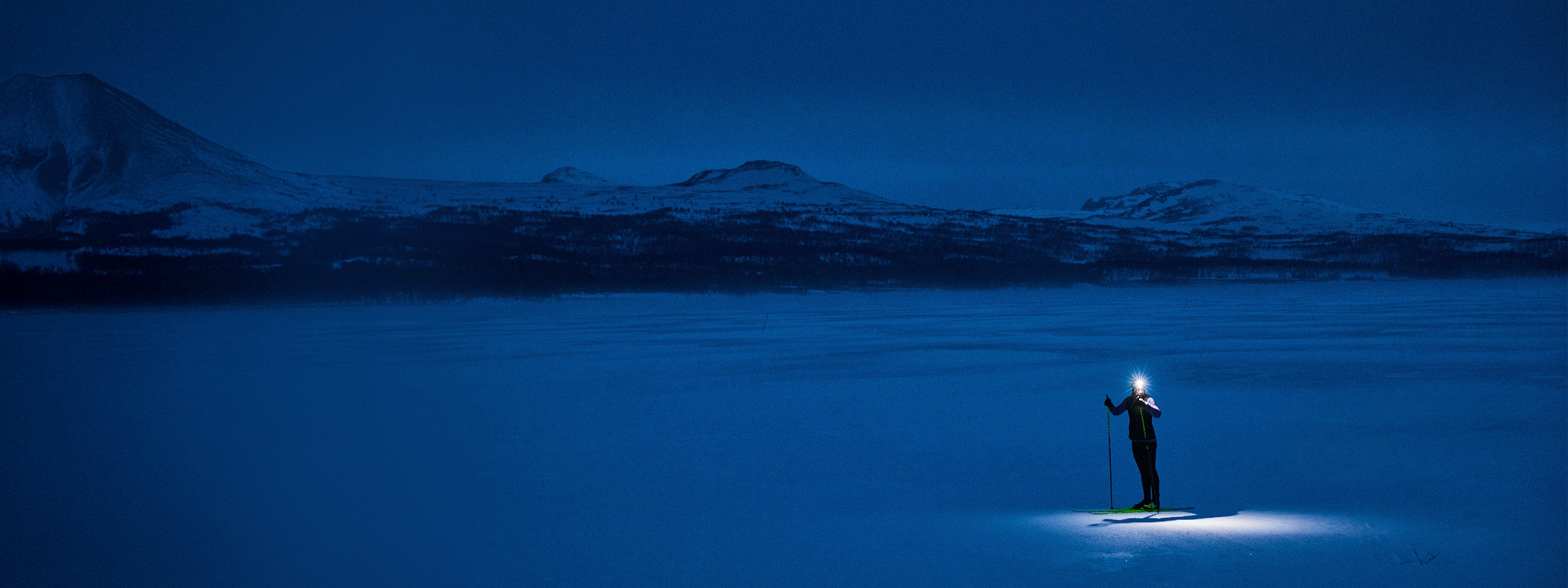 Personne debout sur un lac gelé la nuit, éclairant la neige à l'aide d'une lampe frontale.