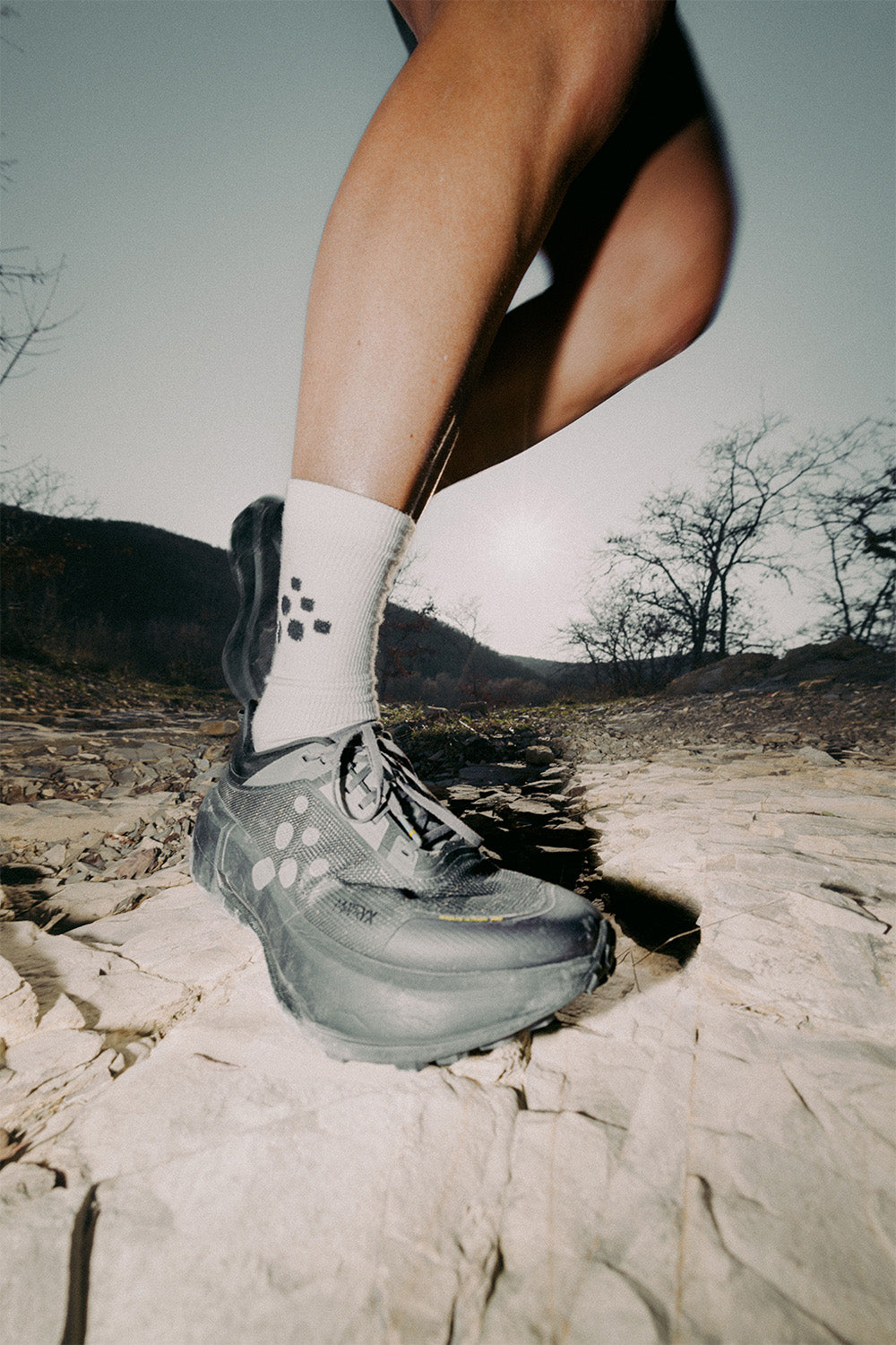 Person wearing hiking shoes on a rocky trail with mountains in the background