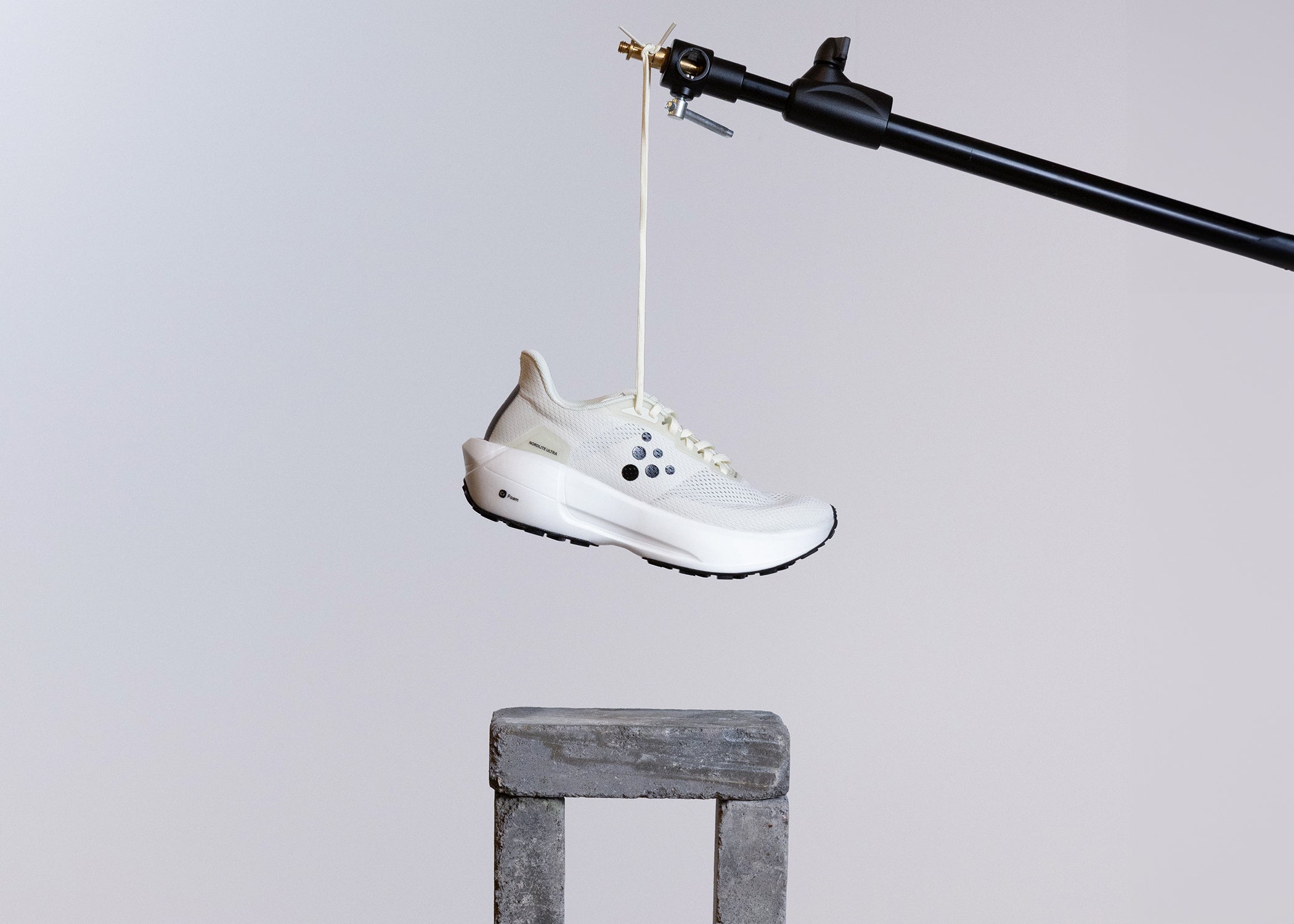 Chaussure blanche suspendue à une corde sur fond gris.