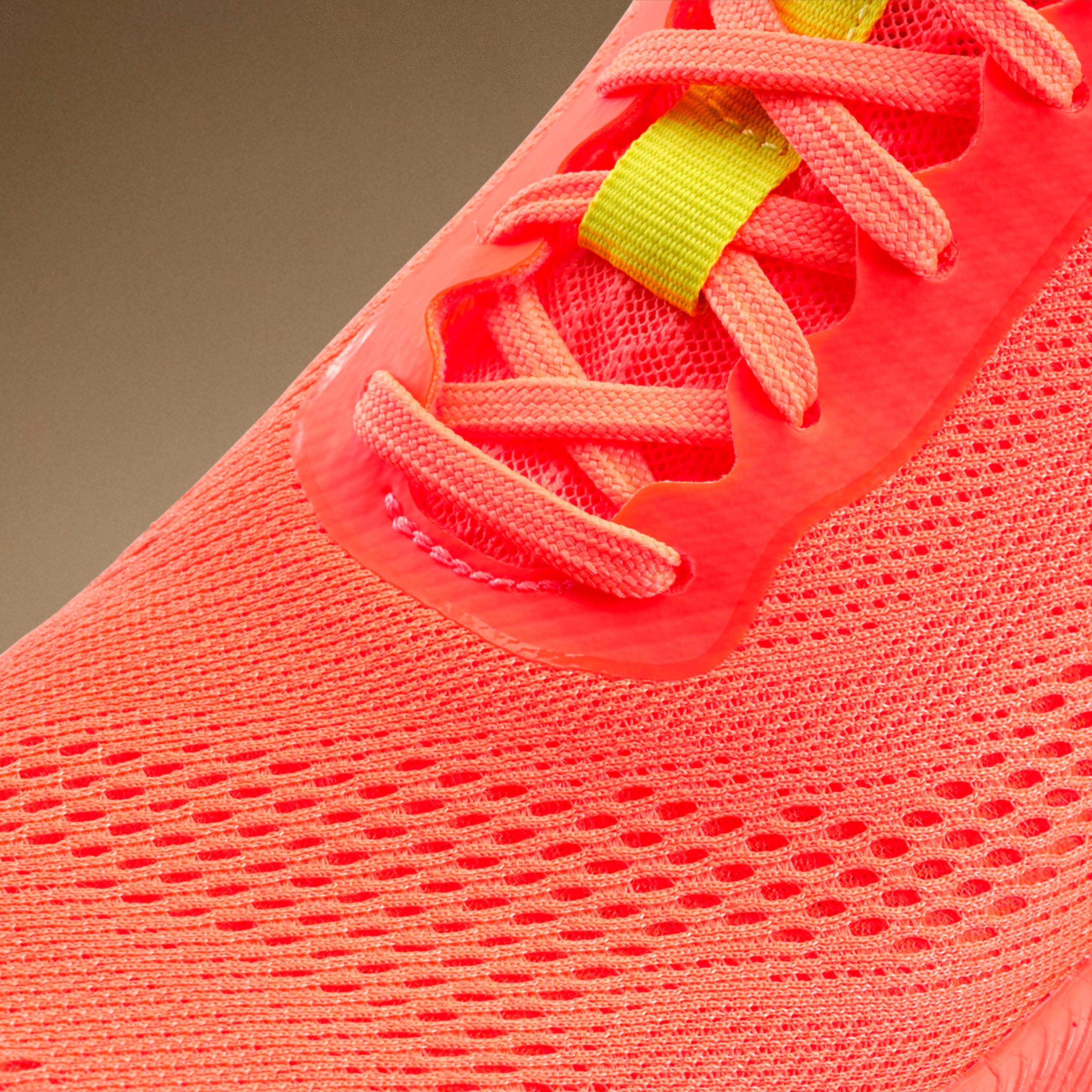 Close-up of a bright orange sneaker with a yellow tag on a beige background