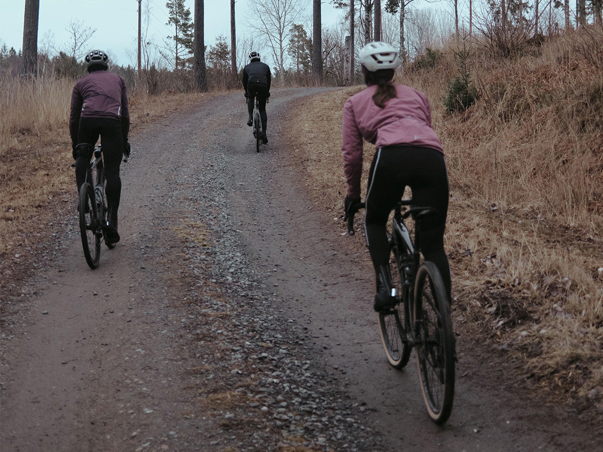 Three people riding bicycles on a dirt path through a forest.