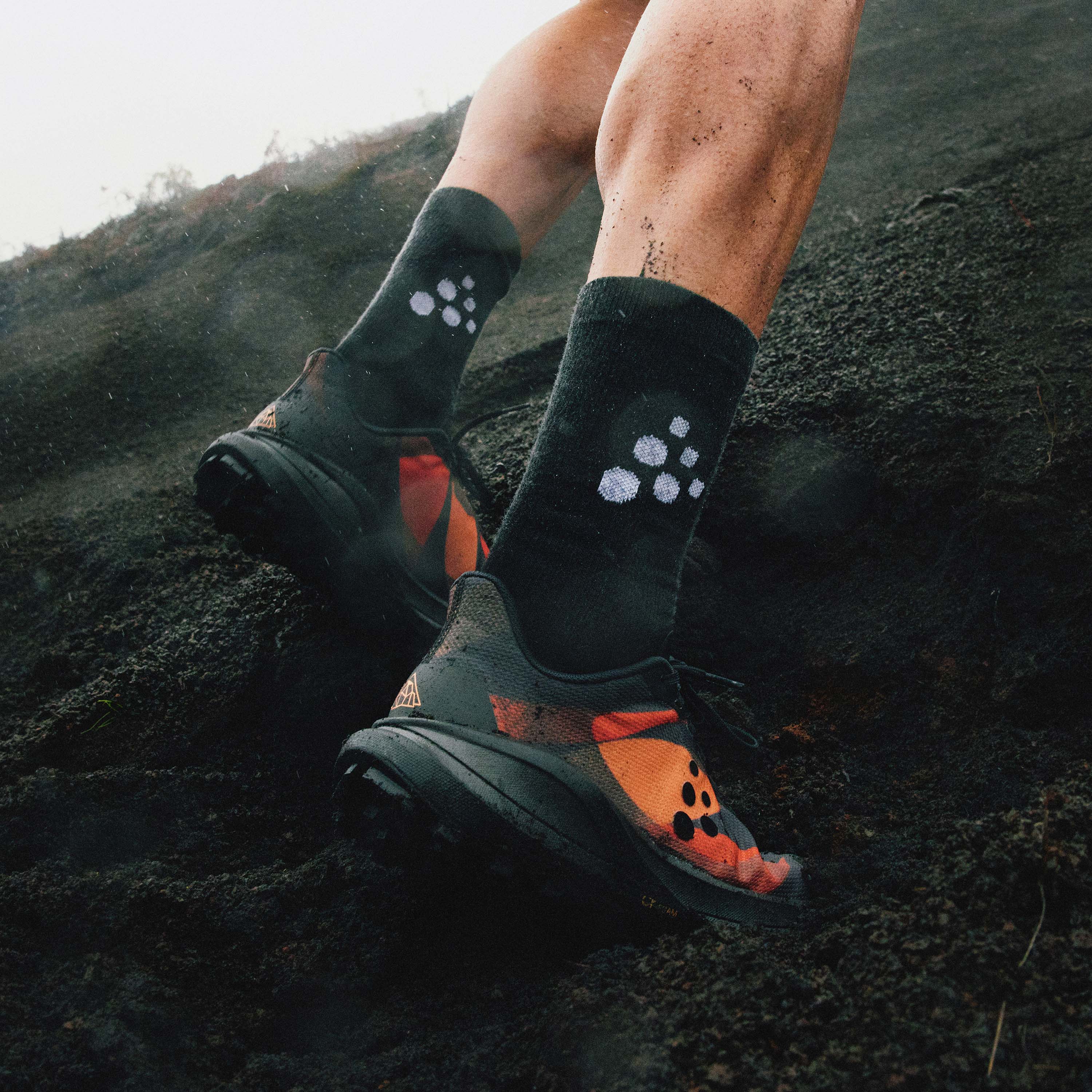 Person wearing black socks orange shoes on a rocky surface.