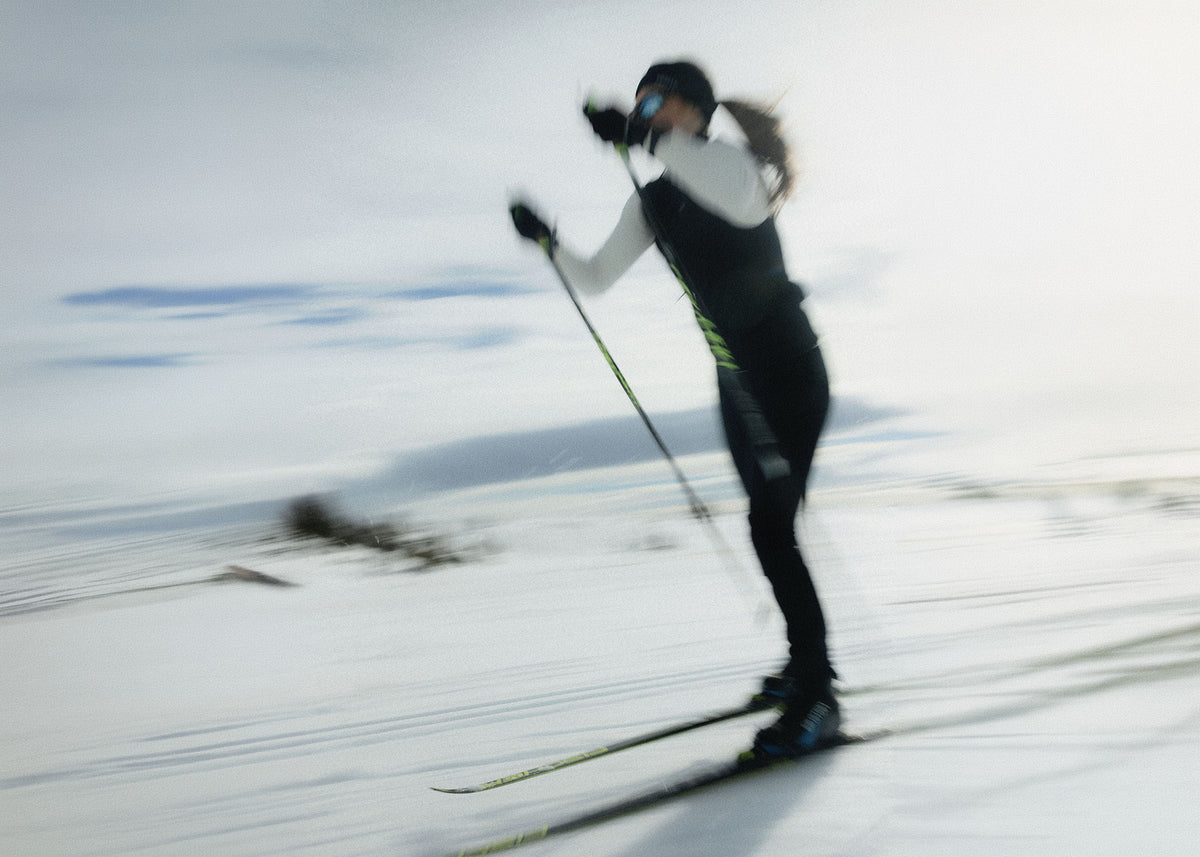 A skier in motion on a snowy slope, wearing a black and white outfit with ski poles and skis, captured with a dynamic motion blur effect.