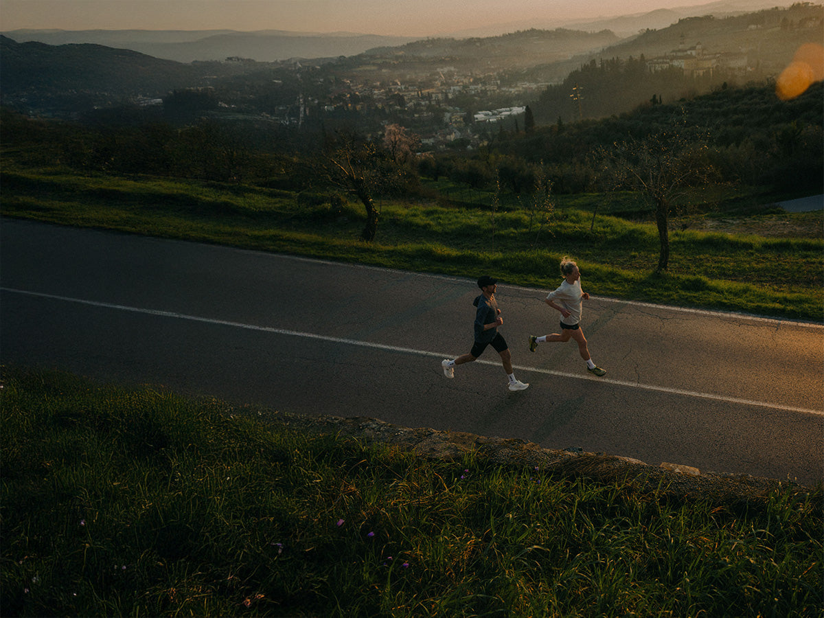 Two runners on a road with a scenic landscape in the background