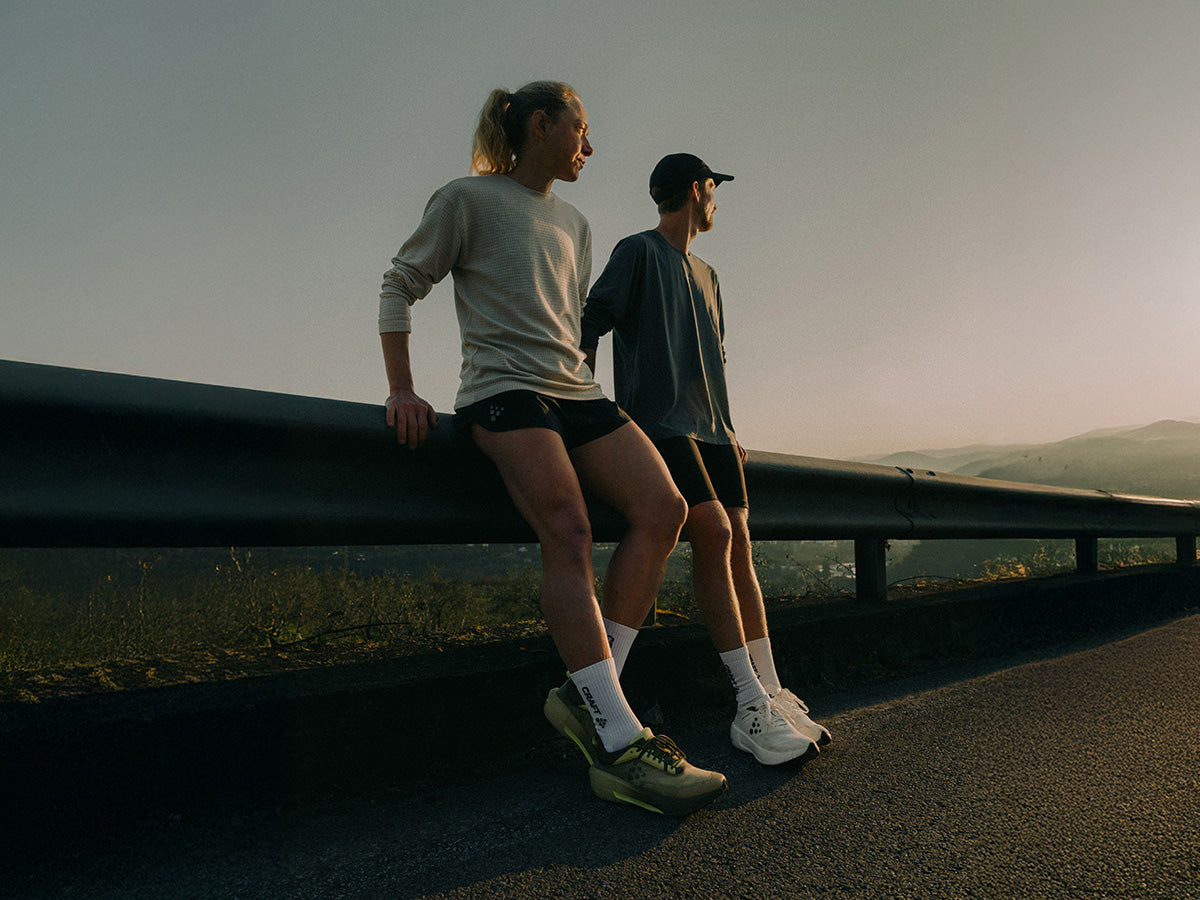 Two people standing on a road overlooking a scenic landscape at sunset.
