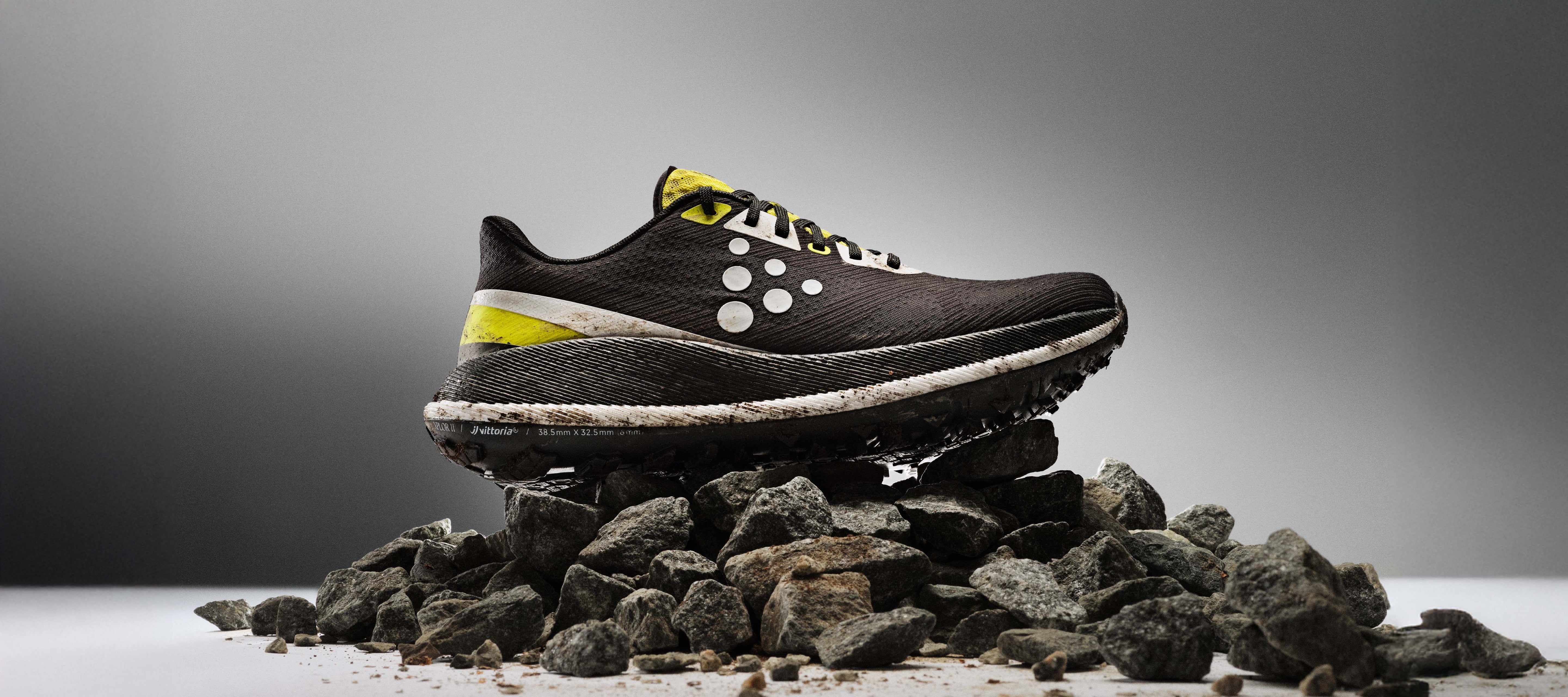 Black running shoe with white sole on a pile of rocks against a gray background